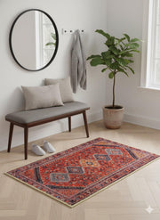2' x 3' Red Blue Geometric Medallion Accent Rug placed / styled in a modern entryway with a wooden bench, round wall mirror, and potted plant.