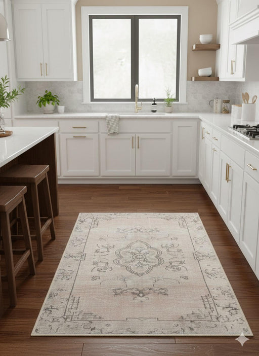 2' x 3' beige and light gray vintage medallion area rug styled on a kitchen floor with white cabinetry and warm wood flooring.