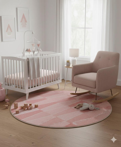 5' Round Blush Ivory & Pale Peach Geometric Modern Area Rug placed in a soft neutral nursery with a white crib, blush rocking chair, light wood floors, and sheer window curtains.