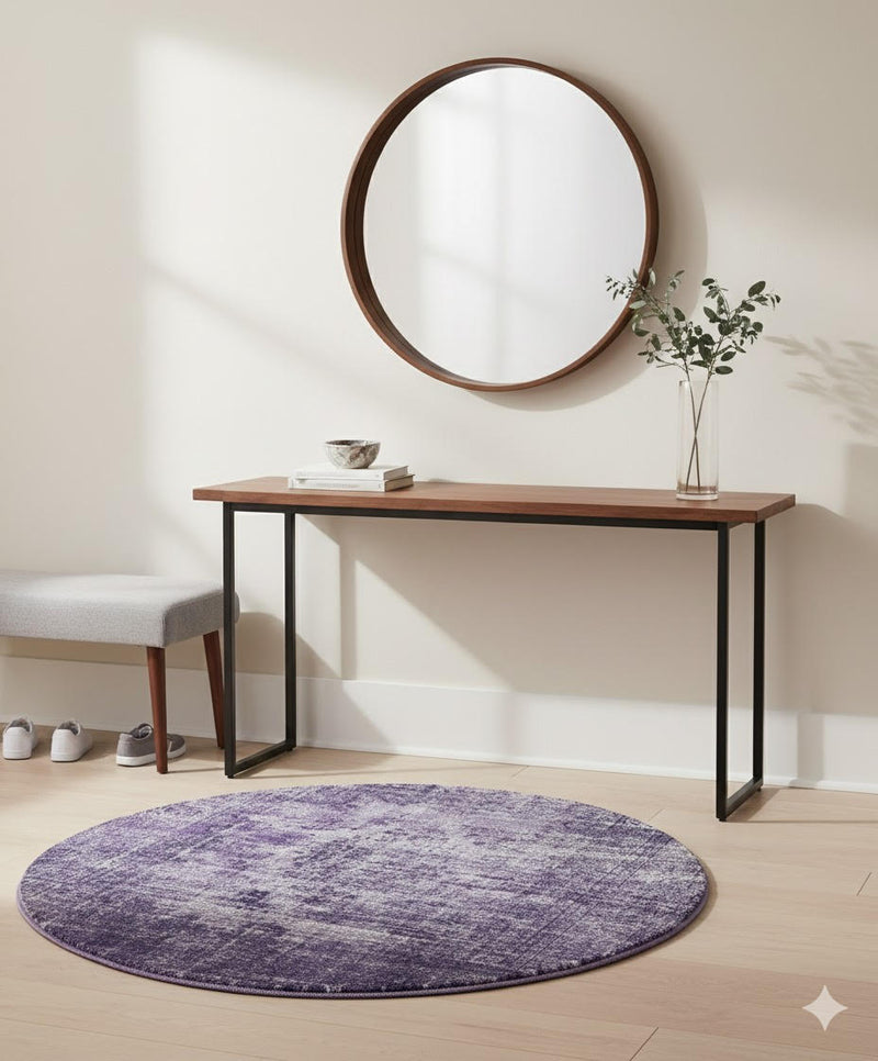 5' Round Purple Plum Soft Gray Round Heathered Abstract/Distressed Modern area rug placed in a minimalist entryway, styled beneath a slim wood console table with black metal legs, a round wall mirror, decorative bowl and greenery, a small bench with shoes, and sunlit neutral walls with light wood flooring.