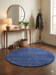 5' round denim blue & soft gold accent minimal motif modern area rug styled in a bright entryway with a wood console table, round mirror, and coat rack.