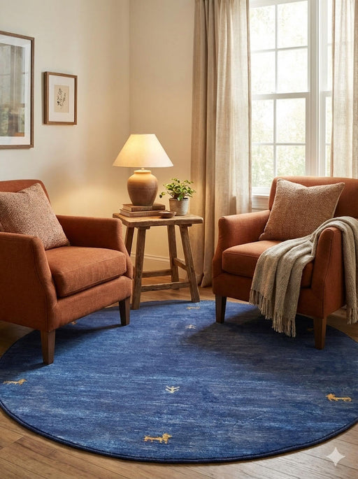 5' round denim blue & soft gold accent minimal motif modern area rug styled in a cozy living room beneath two rust-toned accent chairs and a wooden side table.
