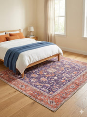 5' x 5' purple and rust soft blue vintage floral square area rug placed beneath a wooden bed in a neutral bedroom with light wood flooring.