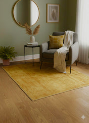 5' x 5' square mustard yellow & warm gold solid modern area rug styled in a cozy living room beneath a gray accent chair with a round mirror, side table, and soft neutral decor.