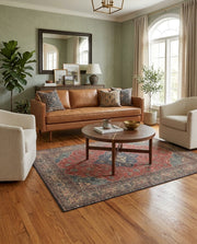 5' x 6' Rectangular Rust Red & Navy Blue Distressed Floral Medallion Traditional Area Rug styled in a living room with a tan leather sofa and round wooden coffee table.