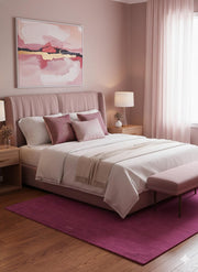 5' x 7' Rectangle Magenta Purple Minimalist Solid Area Rug displayed in a cozy bedroom beneath a bed with neutral bedding and blush pink furnishings.