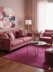5' x 7' Rectangle Magenta Purple Minimalist Solid Area Rug styled in a modern pink-toned living room with a matching sofa, accent chair, round coffee table, and abstract wall art.
