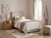 5' x 7' Rectangular Ivory & Gold Blush Geometric Abstract Modern Washable Area Rug placed in a bedroom with a blush upholstered bed and gold-accented nightstand.