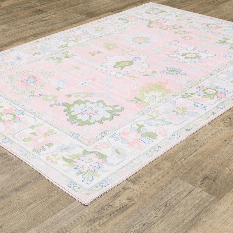 5' x 7' Rectangular Pink Multicolor Floral Traditional Washable Area Rug shown at an angled close-up view, emphasizing its traditional floral border and soft watercolor-inspired design.