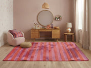 5' x 7' Rectangular Pink & Orange Purple Striped Abstract Modern Area Rug placed in a vanity room with a wooden makeup desk and round mirror.