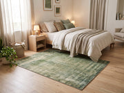 5' x 7' Rectangular Sage Green & Olive Green Distressed Abstract Modern Area Rug placed in a bedroom with a light wood bed frame and white bedding.