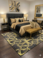 5' x 7' black and gold interlocking geometric rectangular area rug styled in a bedroom with black and gold bedding and dark wood flooring.