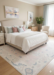 5' x 7' ivory cream and blush pink washable abstract vintage area rug placed in a serene bedroom with a beige upholstered bed, soft pastel pillows, and light wood furniture.