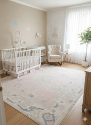 5' x 7' ivory cream blush pink washable abstract vintage area rug styled in a soft nursery space with a white crib, rocking chair, and airy natural light.
