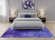 5' x 7' purple soft blue & gray tonal modern abstract rectangular area rug styled in a modern bedroom beneath a platform bed with neutral bedding, matching nightstands, soft lighting, and light wood flooring.