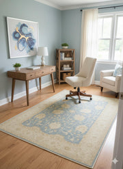 5' x 8' Rectangular Blue & Beige Cream Floral Traditional Area Rug placed in a bright home office with light wood floors, a wooden desk, a cream chair, a small bookshelf, and a window with sheer curtains letting in natural light.