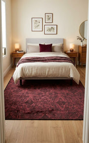 5' x 8' Rectangular Burgundy Red & Black Distressed Geometric Modern Area Rug placed in a bedroom with a cream upholstered bed and wooden nightstands.