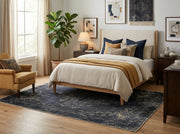 5' x 8' Rectangular Charcoal & Gold Distressed Floral Medallion Vintage Washable Area Rug placed in a bedroom with a wooden bed and mustard accent chair.