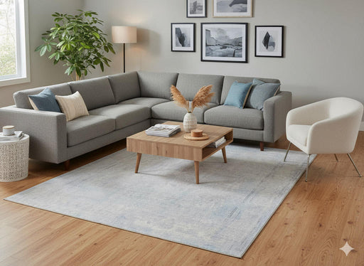 5' x 8' Rectangular Light Gray & Silver Tonal Distressed Solid Modern Minimalist Washable Non-Slip Backing Area Rug styled in a living room with a gray sectional sofa and wooden coffee table.