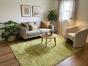 5' x 8' Rectangular Olive Green & Sage Green Distressed Solid Modern Area Rug styled in a living room with a gray sofa and cream accent chair.