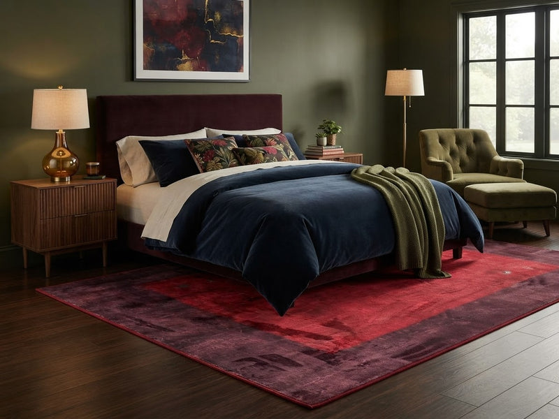 5' x 8' Rectangular Red & Burgundy Distressed Solid Border Modern Area Rug placed in a bedroom with a burgundy upholstered bed and navy bedding.