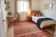 5' x 8' Rectangular Rust Red & Navy Blue Striped Tribal Southwestern Area Rug placed in a bedroom with a wooden bed and navy blue blanket.