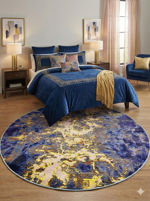 6-foot round navy blue and gold abstract modern area rug placed beneath a bed in a stylish bedroom with blue bedding and gold accents.