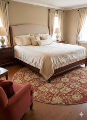 6 ft round red, beige, and cream floral medallion traditional area rug placed partially under a bed in a traditional bedroom with neutral bedding and wood furniture.