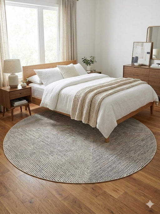 6' round  creamy ivory light gray herringbone textured modern area rug styled at the foot of a bed in a warm neutral bedroom.