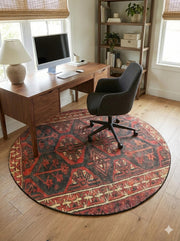 6' round deep rust red and charcoal black southwestern geometric area rug placed under a wooden desk in a bright home office.