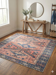 6' x 6' square blue and rust Southwestern geometric washable area rug placed in an entryway with a wood console table, round mirror, and neutral décor.