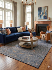 6' x 6' square blue gray distressed washable area rug styled in a cozy living room with a navy sectional sofa, leather accent chair, and round wood coffee table.