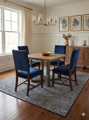 6' x 6' square blue gray modern distressed washable area rug placed under a rustic wooden dining table with navy upholstered chairs.