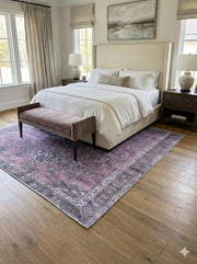 6' x 6' square purple and charcoal distressed medallion area rug placed partially under a bed in a neutral bedroom setting.