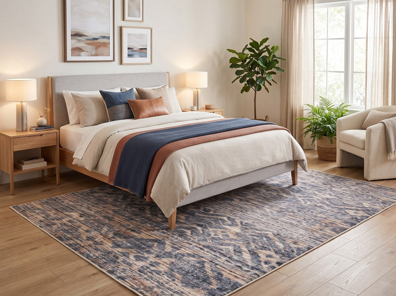 6' x 9' Rectangular Blue Beige Distressed Geometric Tribal Southwestern Area Rug placed in a cozy bedroom with a wooden bed, white bedding, blue and rust accent pillows, and a cream upholstered chair.