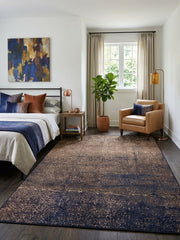 6' x 9' Rectangular Brown Navy Crackled Geometric Modern Area Rug placed in a bedroom with a black metal bed frame, white bedding, navy blue throw, and tan leather accent chair.