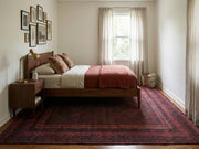 6' x 9' Rectangular Burgundy Black Distressed Geometric Tribal Traditional Area Rug styled in a bedroom with a wooden bed and pink bedding.