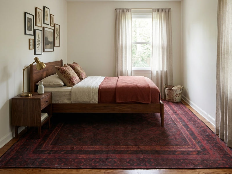 6' x 9' Rectangular Burgundy Black Distressed Geometric Tribal Traditional Area Rug styled in a bedroom with a wooden bed and pink bedding.