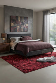 6' x 9' Rectangular Burgundy Red Abstract Geometric Modern Area Rug styled in a bedroom with a dark gray upholstered bed and burgundy bedding.