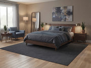 6' x 9' Rectangular Charcoal Gray Black Solid Textured Modern Minimalist Washable Area Rug styled in a bedroom with a wooden bed and gray bedding.