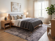 6' x 9' Rectangular Charcoal Gray Silver Distressed Abstract Modern Area Rug placed in a bedroom with a gray upholstered bed, white bedding, charcoal gray blanket, and wooden nightstands.