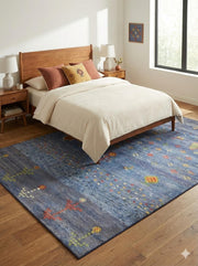 6' x 9' blue multi-color abstract geometric modern area rug positioned under a bed in a neutral bedroom setting.