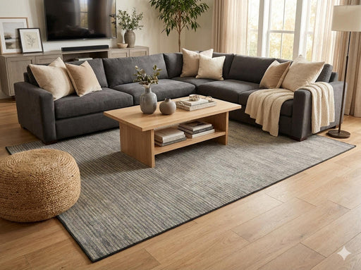 6' x 9' gray and beige solid modern washable area rug placed in a contemporary living room with a charcoal sectional sofa, wood coffee table, and warm neutral decor.