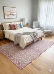 6' x 9' rose pink, teal, and ivory geometric transitional rectangular area rug styled partially under a bed in a light bedroom with neutral bedding and pastel accents.