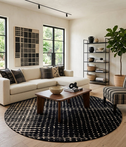 7' Round Black Ivory Abstract Geometric Modern Washable Area Rug styled in a living room with a cream sectional sofa and wooden coffee table.