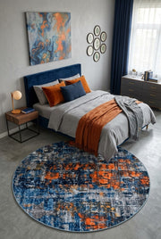 7' Round Navy Blue Orange Gray Distressed Abstract Modern Area Rug placed in a bedroom with a navy upholstered bed and orange accent pillows.