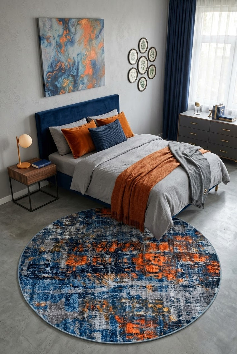 7' Round Navy Blue Orange Gray Distressed Abstract Modern Area Rug placed in a bedroom with a navy upholstered bed and orange accent pillows.