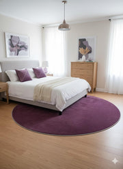 7' Round Purple Deep Violet Undertones Solid Modern Area Rug placed / styled in a bright modern bedroom beneath a queen-sized bed with light wood furniture and coordinating purple accent pillows.