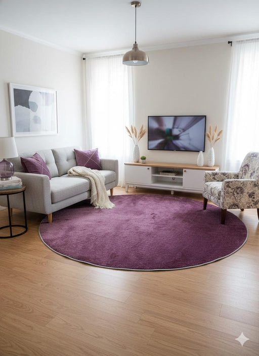 7' Round Purple Deep Violet Undertones Solid Modern Area Rug placed / styled in a modern living room centered under a gray sofa and accent chair with a TV console backdrop.