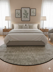 7' round beige, ivory, taupe, and gray heathered washable area rug placed beneath a modern bed in a calm, minimalist bedroom with neutral furnishings.